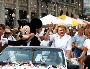 Barbara Taylor Bradford and Mickey Mouse acknowledge the large crowd from an open motorcade at Walt Disney World in Florida, as confetti showers them on the parade route.
